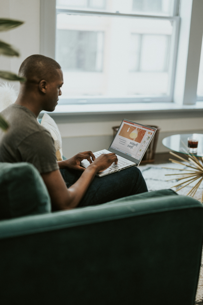 A man in casual attire working on a laptop in his living room.