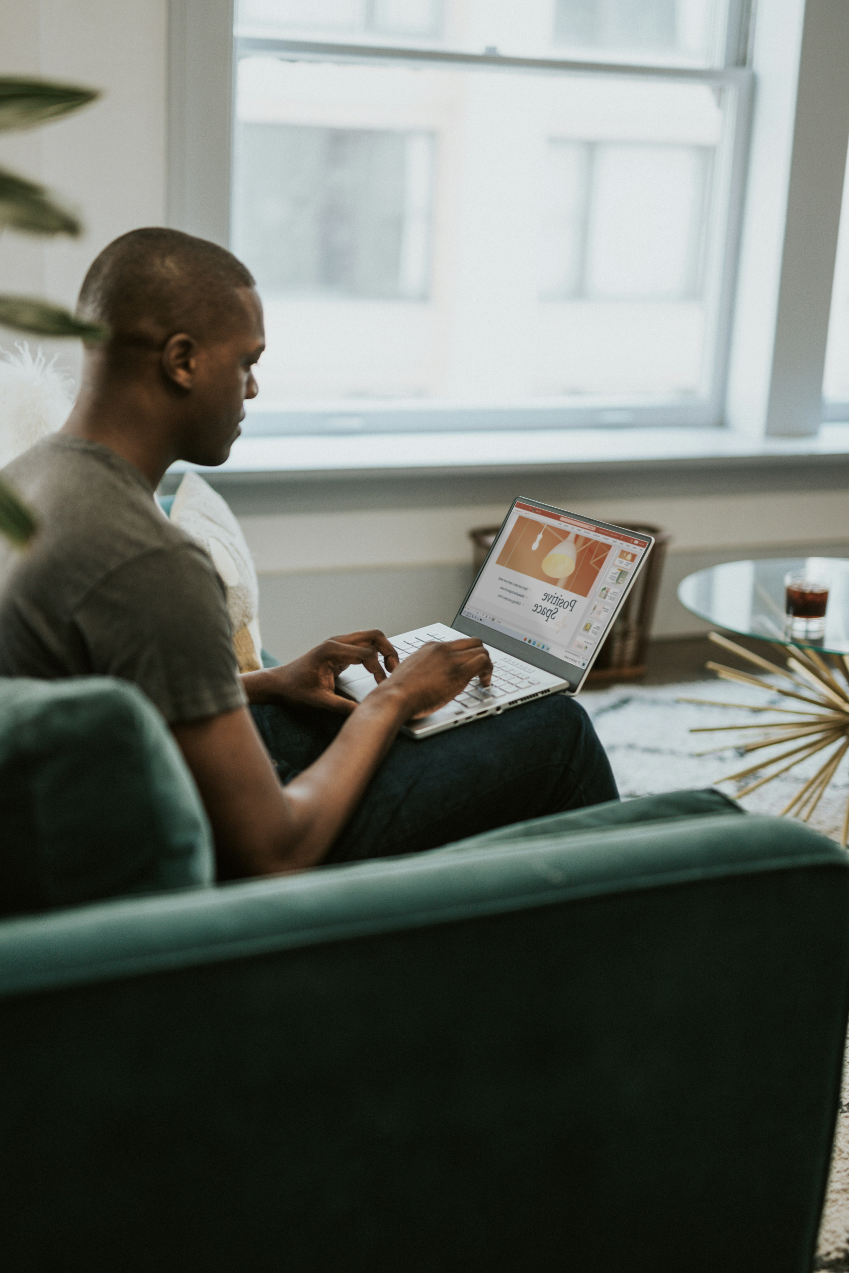 A man in casual attire working on a laptop in his living room.
