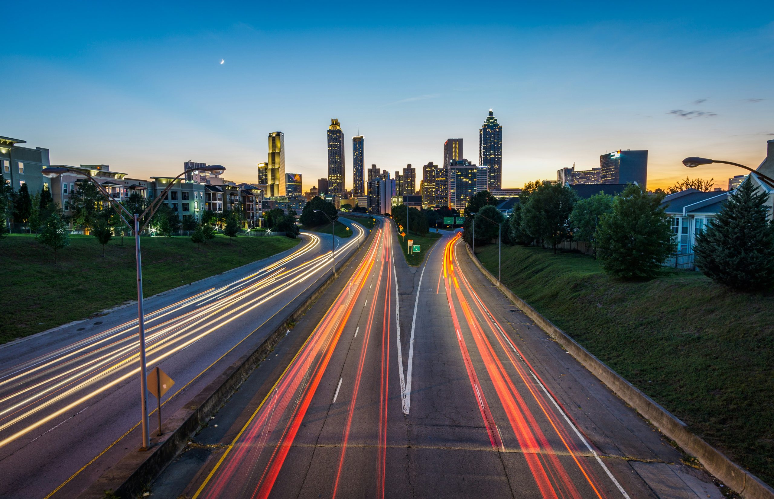An evening view of the skyline of the Atlanta business district, foregrounded by cars headed into the city from the highway.